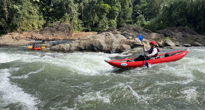 A person wearing safety gear paddles a watercraft through small rapids